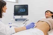 Crop medical practitioner making sonogram to happy pregnant woman during work in contemporary fertility clinic — Stock Photo