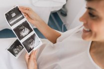 Зверху вагітна жінка оглядає фотографію сонограми, сидячи в кріслі в палаті сучасної клініки фертильності — стокове фото