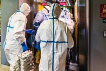 Grupo de médicos irreconocibles que usan uniforme protector mientras toman pacientes con virus del ascensor en el hospital - foto de stock