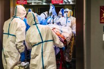 Gruppe unkenntlich gemachter Ärzte trägt Schutzuniform, während sie Patienten mit Virus aus dem Aufzug ins Krankenhaus bringen — Stockfoto