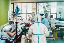 Médecins professionnels méconnaissables en uniformes de protection et masques prenant soin du patient infecté par le virus alors qu'il se tenait dans la salle d'opération de l'hôpital moderne — Photo de stock