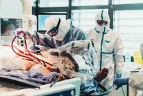 Unerkennbare Berufsärzte in Schutzuniformen und Masken kümmern sich im Operationssaal eines modernen Krankenhauses um einen Patienten mit Virusinfektion — Stockfoto