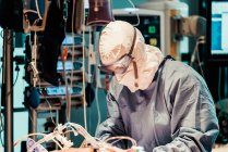 Побічний погляд на невпізнаваного професійного лікаря в захисній формі та масках, який піклується про пацієнта з вірусною інфекцією, стоячи в операційній кімнаті в сучасній лікарні — стокове фото