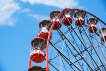 De baixo da roda gigante com cabines vermelhas localizadas no parque de diversões no dia ensolarado com céu azul — Fotografia de Stock