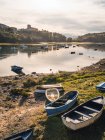 Старые потрепанные деревянные рыбацкие лодки, плавающие на воде мирного озера и размещенные на травянистом берегу — стоковое фото