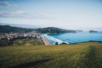 Scenic view of green hill, distant village and ocean — Stock Photo
