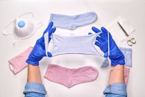 Pessoa anônima em luvas estéreis azuis mostrando como fazer máscara facial usando meias enquanto estiver em casa durante o período de quarentena do coronavírus — Fotografia de Stock