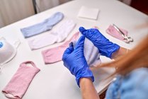 Анонимный человек в синих стерильных перчатках показывает, как сделать маску для лица с помощью носков, находясь дома во время карантинного периода коронавируса — стоковое фото