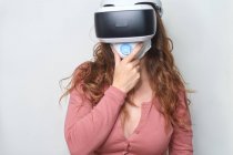 Анонімні жінки з рудим волоссям торкаються маски обличчя, відчуваючи віртуальну реальність, використовуючи сучасні навушники під час карантину. — стокове фото