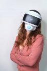 Mulher anônima com cabelos vermelhos usando máscara facial enquanto experimenta realidade virtual usando headset moderno durante o tempo de quarentena do coronavírus — Fotografia de Stock