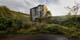 Vista ad ampio angolo di solitario edificio industriale in pietra invecchiata con pareti grigie squallide situate tra cespugli verdi contro il cielo nuvoloso nelle Asturie in Spagna — Foto stock