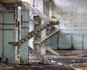 Paredes de concreto e restos de escadas no antigo edifício industrial abandonado com chão bagunçado — Fotografia de Stock