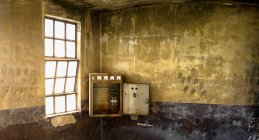 Caixa velha do interruptor instalada no canto da sala weathered com paredes de pedra shabby e janela com grade dentro do edifício industrial desolado — Fotografia de Stock