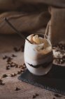 Glas leckerer Sahnekaffee-Nachtisch mit Löffel auf schwarzer Oberfläche serviert mit Kaffeebohnen auf Holztisch — Stockfoto
