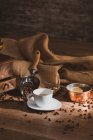 Café preto fresco em copo de cerâmica branca colocado no pires perto do moedor de café e grãos de café na mesa de madeira — Fotografia de Stock