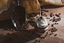 Ein Glas süßes Dessert mit Schokolade und Kaffee garniert mit Sahne auf einem Holztisch in der Nähe einer Metallschaufel mit Kaffeebohnen — Stockfoto