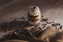 Склянка смачного вершкового кавового десерту з ложкою, поданою на чорній поверхні з кавовими зернами на дерев'яному столі — стокове фото