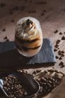 Стекло вкусного сливочного кофе десерт с ложкой подается на черной поверхности с кофейными зернами на деревянный стол — стоковое фото