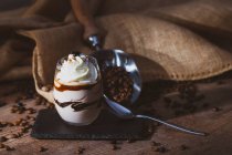 Стекло сладкого десерта с шоколадом и кофе, украшенное кремом, помещенным на деревянный стол рядом с металлическим сенсатором с кофейными зёрнами — стоковое фото