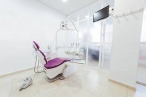 Інтер'єр сучасного легкого порожнього стоматологічного кабінету зі стільцем та медичними інструментами та обладнанням, розміщеними навколо та білою раковиною біля стіни — стокове фото