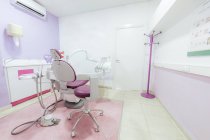 Інтер'єр сучасного легкого порожнього стоматологічного кабінету зі стільцем та медичними інструментами та обладнанням, розміщеними навколо та білою раковиною біля стіни — стокове фото
