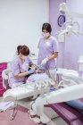 Dentiste féminine en uniforme et masque durcissant les dents du patient avec une assistante féminine dans une clinique dentaire moderne — Photo de stock