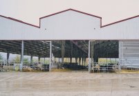 Granero de vacas con valla de metal y puestos bajo techo de metal con patio cercano situado en la granja moderna en el campo - foto de stock