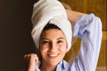 Smiling female with white terry towel on head standing leaned on hand and looking at camera in flat on sunny day — Stock Photo