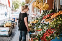 Side view of positive female in casual wear and sunglasses standing near fruit counter in Turkish market and exploring goods while walking through streets of city — Stock Photo