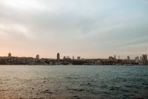 Paesaggio pittoresco della città remota con grattacieli che si trovano vicino al mare mozzafiato e cielo viola tramonto con soffici nuvole in serata — Foto stock