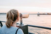 Visão traseira de viajante feminino anônimo em traje casual em pé no dique e admirando a vista do pôr do sol incrível colorido — Fotografia de Stock