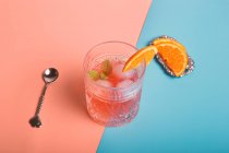 Вид зверху на алкогольний коктейль з кубиками льоду і гілочкою м'яти в склі, розміщеному на барвистому фоні з апельсиновими скибочками — стокове фото
