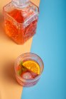 Cóctel de naranja fría fresca en jarra y taza de vidrio con cubitos de hielo - foto de stock