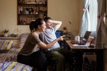 Молода пара в повсякденному одязі, сидячи в спальні за столом і використовуючи комп'ютер разом під час обговорення відео — стокове фото