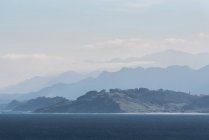 Pintoresca costa rodeada de colinas y montañas rocosas cubiertas de niebla y nubes - foto de stock