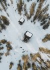 Vue aérienne de petites cabanes de bûcherons situées dans la forêt de pins neigeux — Photo de stock