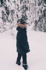Vista lateral de una viajera femenina irreconocible en ropa interior cálida parada en un sendero nevado entre abetos cubiertos de nieve en el día de invierno en Finlandia - foto de stock