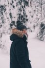 Seitenansicht einer unkenntlichen Reisenden in warmer Oberbekleidung, die an einem Wintertag in Finnland auf einem schneebedeckten Pfad zwischen schneebedeckten Fichten steht — Stockfoto