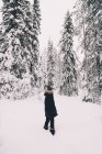 Side view of unrecognizable female traveler in warm outerwear standing on snowy path among snow covered spruce trees in winter day in Finland — Stock Photo