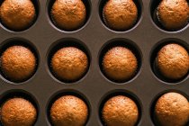 Draufsicht auf köstlichen Muffin in Papierschachtel auf Tablett auf Holztisch in der Küche platziert — Stockfoto