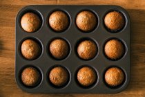Vista superior do delicioso muffin na caixa de papel na bandeja colocada na mesa de madeira na cozinha — Fotografia de Stock