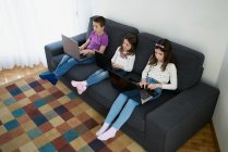 Gruppo di bambini che usano i computer portatili seduti sul divano di casa — Foto stock