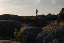 Силуэт вида сбоку женщины-туристки с рюкзаком, стоящим на скалистом склоне холма с фотокамерой, любующейся красивым пейзажем в пасмурный день — стоковое фото