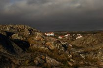 Скалистый пейзаж с деревенскими домами в солнечном свете и темном облачном небе — стоковое фото