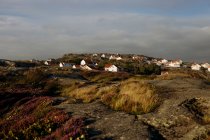 Pittoresca vista del paesaggio tranquillo con scogliere rocciose solitarie con erba verde e fiori e case situate su colline rocciose nella giornata nuvolosa — Foto stock