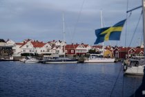 Puerto de yates con yates blancos aparcamiento en el muelle en aguas tranquilas del mar sobre el fondo de la pequeña ciudad costera con bonitas casas y cielo nublado en Suecia - foto de stock