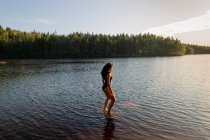 Зверху тонка жінка в купальнику стоїть у спокійній воді озера, насолоджуючись заходом сонця і величними пейзажами — стокове фото