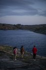 Back view of anonymous traveler couple in casual outfit with photo cameras in hands walking down rocky coast to sea and admiring amazing view — Stock Photo