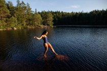 Сверху вид на стройную женщину в купальнике, стоящую в спокойной воде озера, наслаждаясь закатом и величественными пейзажами — стоковое фото