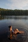 Зверху тонка жінка в купальнику сидить із закритими очима у спокійній воді озера, насолоджуючись заходом сонця та величними пейзажами — стокове фото